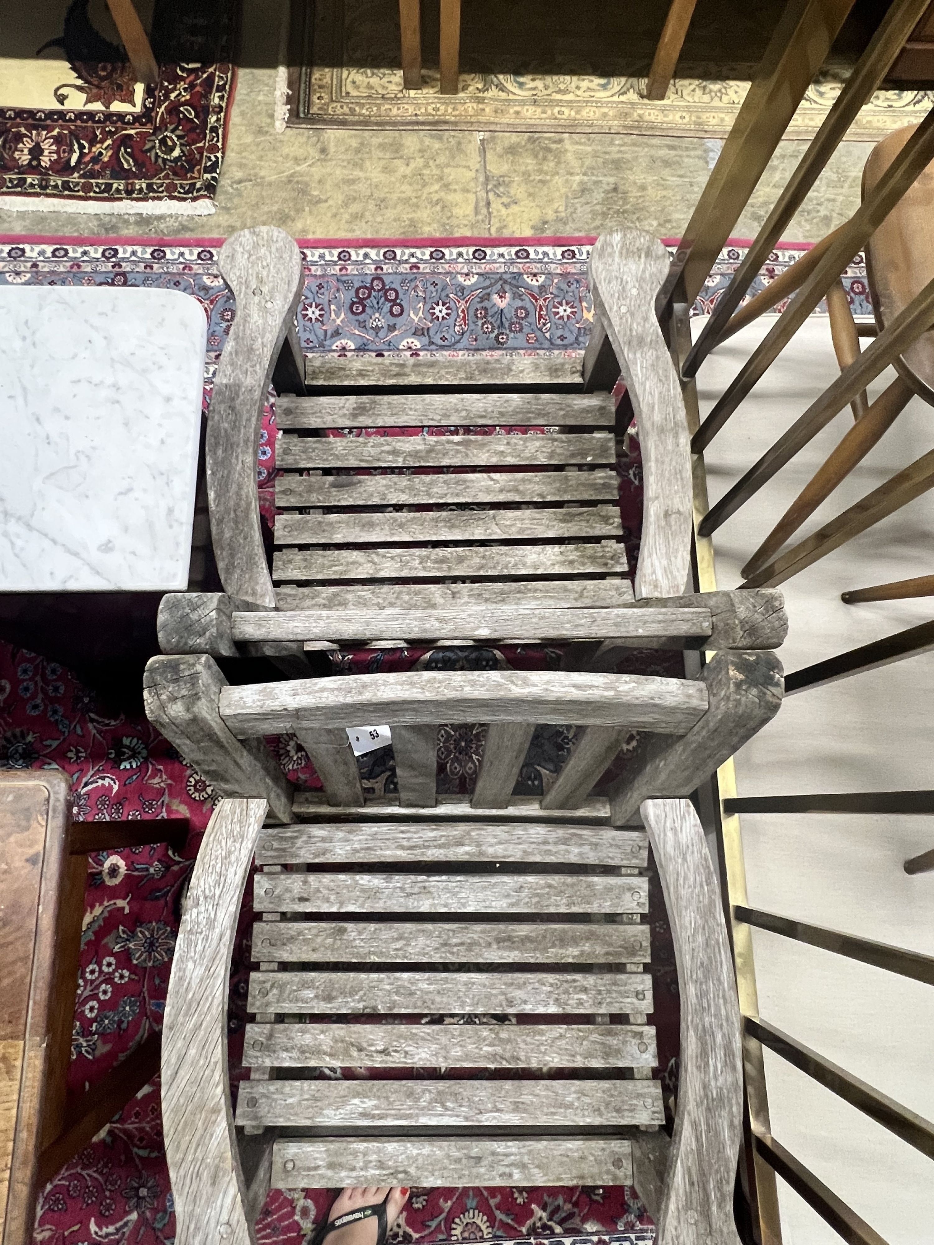 A pair of weathered teak slatted garden elbow chairs, width 64cm depth 60cm height 86cm